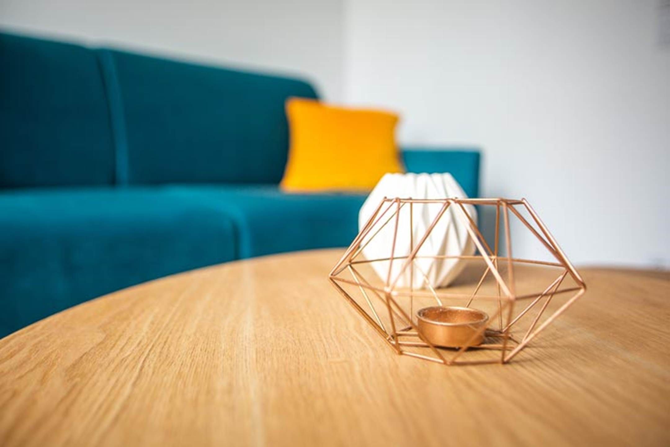 A geometric metal sculpture on a wooden table with a blue sofa and a yellow pillow in the background.