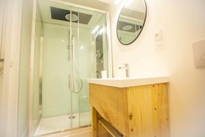Een badkamer met een douchecabine van glas, een houten wastafelmeubel en een ronde spiegel.