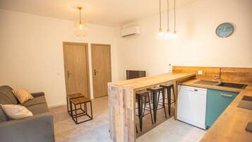 Une cuisine compacte avec un îlot central en bois, des tabourets de bar, un lave-vaisselle et une horloge au mur.