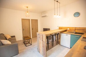 A compact kitchen with a wooden island, bar stools, a dishwasher, and a clock on the wall. - Rare T2 with terrace and spa at the foot of the castle (Montignac)