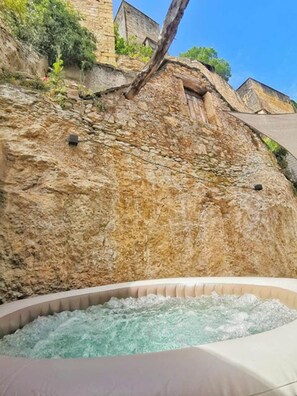 Un jacuzzi con un muro de piedra de fondo y un cielo despejado.