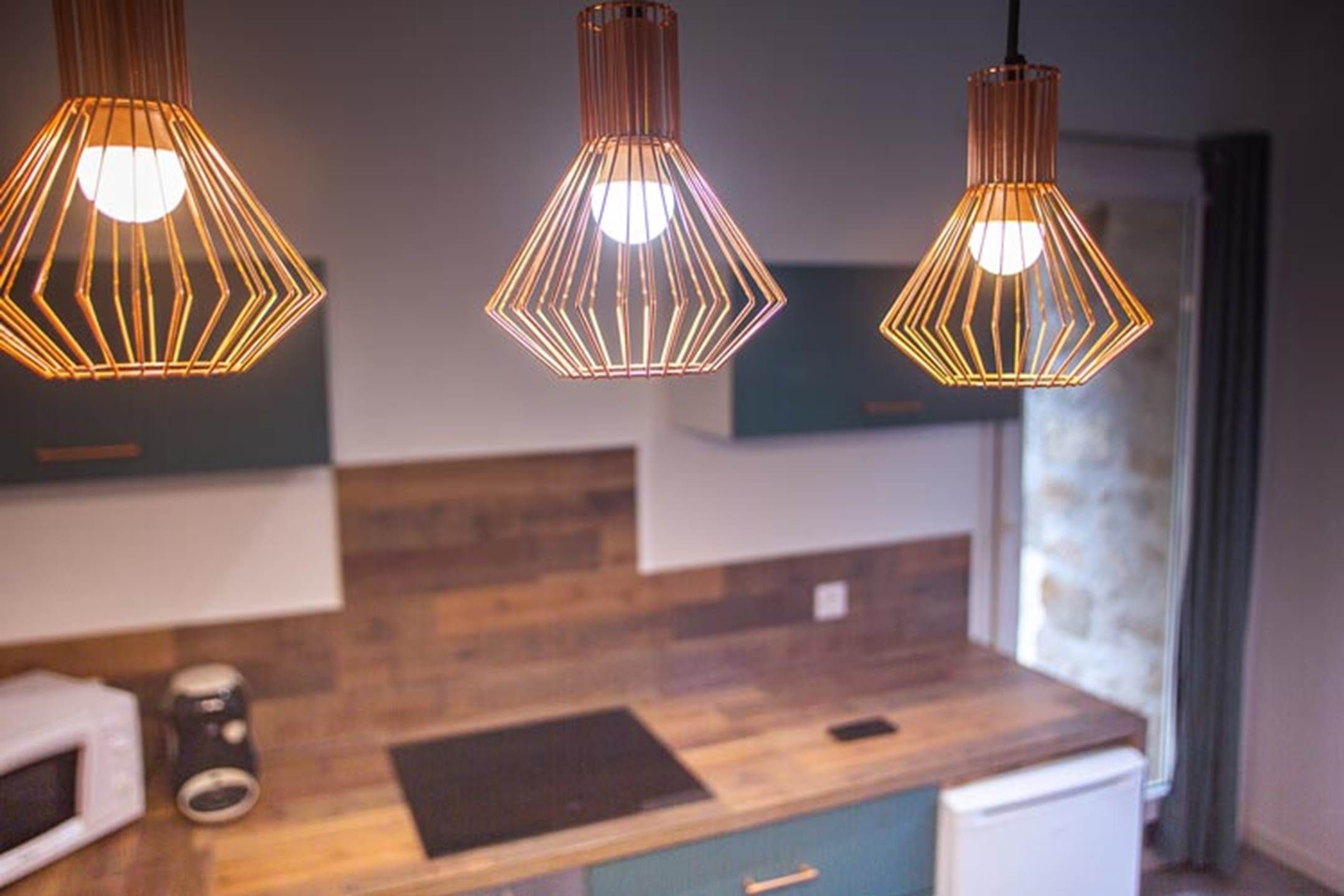 A modern kitchen with wooden countertops, a microwave, and three pendant lights with a geometric design.