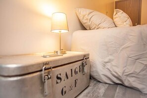 A bed with a white duvet, a bedside lamp, and a suitcase with the text 'SAIGE G & F' on it.