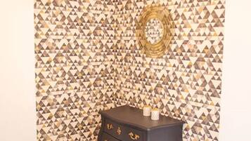 Una habitación de esquina con un papel tapiz estampado, una mesita de noche de madera oscura con cajones y suelo de madera.