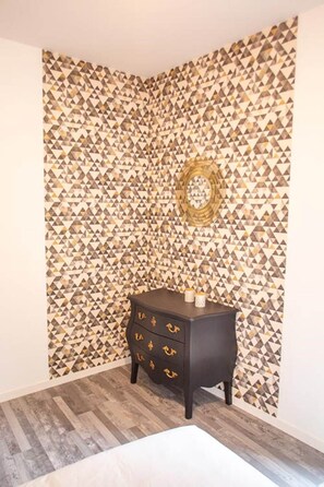 A corner room with a patterned wall, a dark wooden side table with drawers, and a wooden floor. - Rare T2 with terrace and spa at the foot of the castle (Montignac)