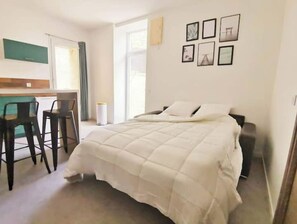 A hotel room with a bed, a desk, and chairs. There are framed pictures on the wall.