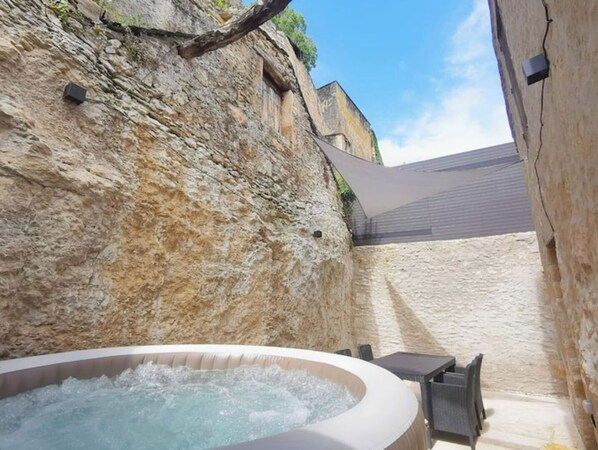 A hot tub in a stone-walled courtyard with a table and chairs.