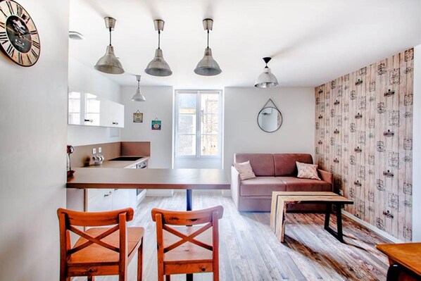 A modern kitchen with a central island, a dining area with wooden chairs, a sofa, and a coffee table.