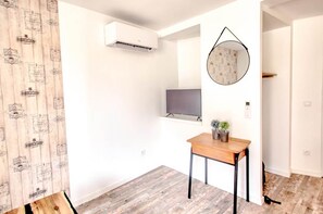 Ein Zimmer mit Holzboden, einem Schreibtisch mit Stuhl, einem Wandfernseher und einer Klimaanlage.