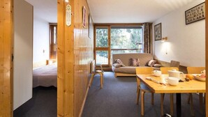 A cozy room with a wooden floor, a sofa, a dining table with chairs, and a window with a view of trees. - 50m from resort center, 6th floor, balcony, 40m², Les Arcs (Les Arcs)