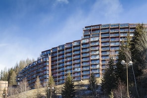 A multi-story hotel with a modern architectural design, featuring numerous balconies and a clear view of the surrounding landscape.