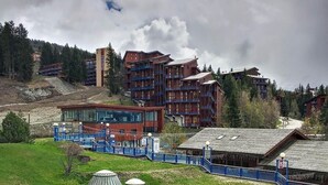 Il s’agit d’un hôtel composé de plusieurs bâtiments, dont une structure rouge dotée de balcons et un bâtiment bleu à la façade en verre. On peut également observer plusieurs structures coniques sur la pelouse.