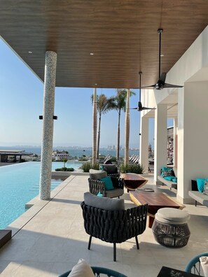 Zona junto a la piscina con mobiliario, vista al océano y palmeras.