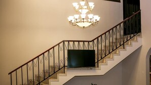 Un escalier avec une rampe noire, un lustre et un téléviseur à écran plat fixé au mur.