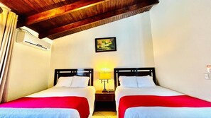 Una habitación con dos camas, una mesita de noche con lámpara, un cuadro en la pared y un equipo de aire acondicionado.