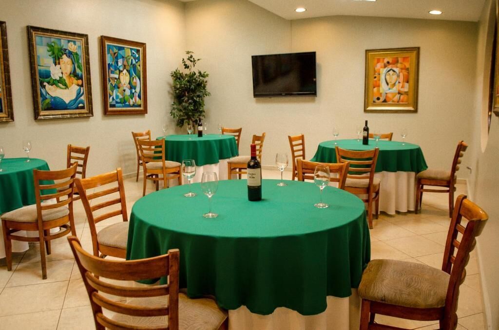 Un comedor con mesas redondas cubiertas con manteles verdes, sillas de madera y un televisor montado en la pared.