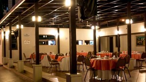 Un espace de restauration en plein air, avec des tables dressées pour les clients, protégé par une structure de toit, et un escalier menant à un niveau supérieur.