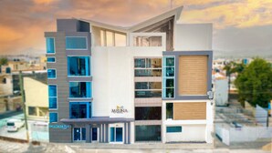 A modern hotel with a prominent 'Melina Hotel' sign, multiple balconies, and a view of the cityscape. - Melina Hotel (Higuey)