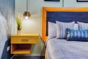 A bedroom with a bed, a nightstand, a hanging light, and a potted plant.