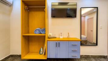 Une chambre dotée d’une armoire en bois, d’un téléviseur à écran plat, d’un miroir et d’une petite table sur laquelle sont posés des articles de toilette.
