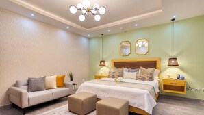 A modern bedroom with a large bed, a sofa, two ottomans, a nightstand, and a wall-mounted mirror. - Melina Hotel (Higuey)