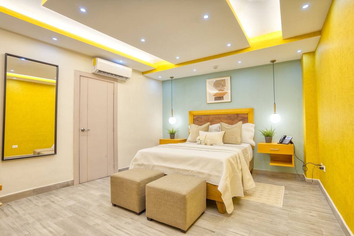 A modern bedroom with a bed, bedside tables, a mirror, and a small plant.
