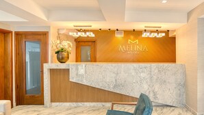 A hotel reception area with a marble counter, a wooden reception desk, a blue chair, and a vase of flowers. - Melina Hotel (Higuey)