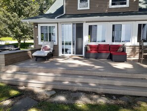 A covered deck with outdoor seating, including a chair and a sofa with red cushions.