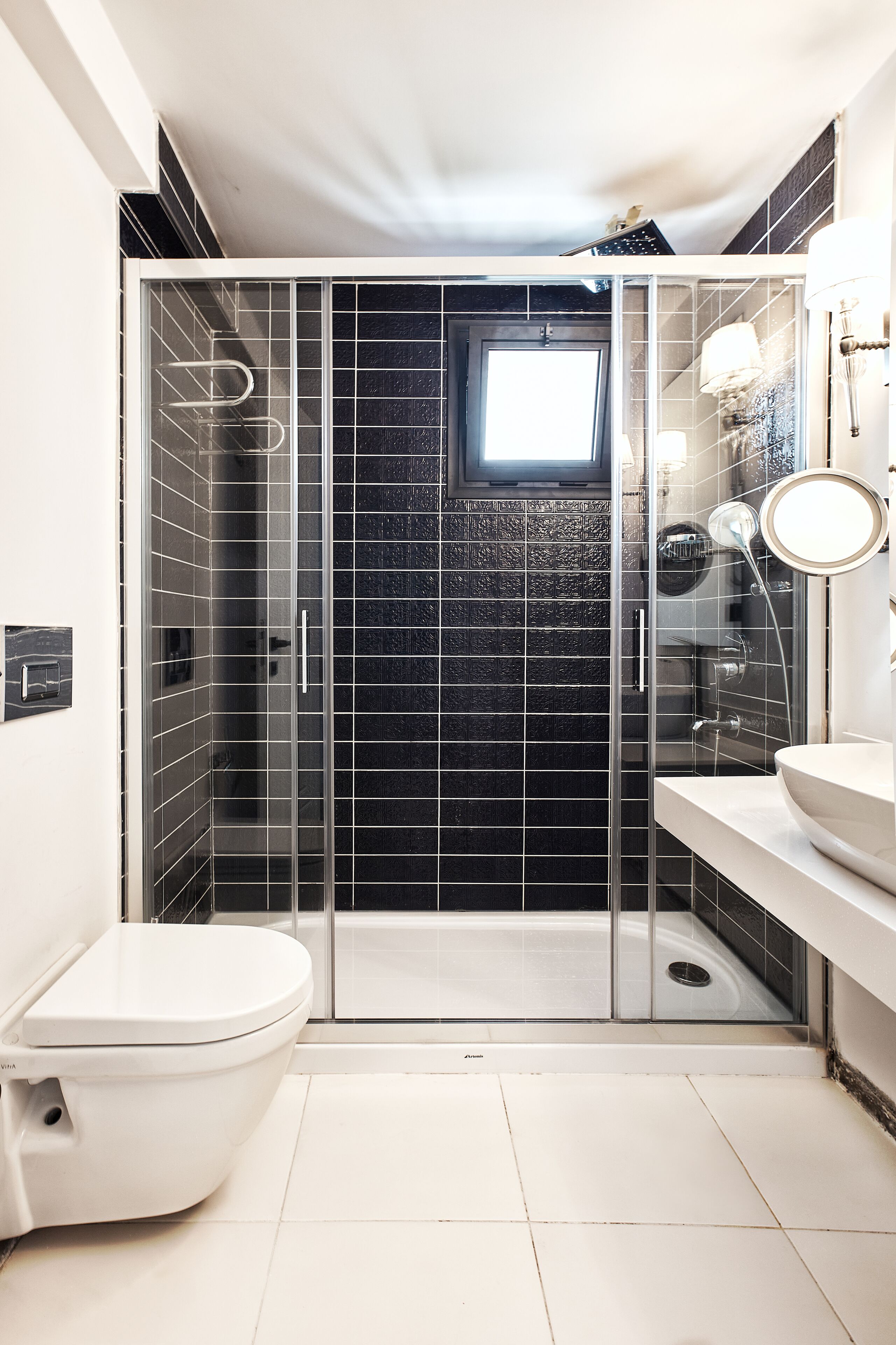 A modern bathroom with a glass-enclosed shower, a white toilet, and a sink with a round mirror.