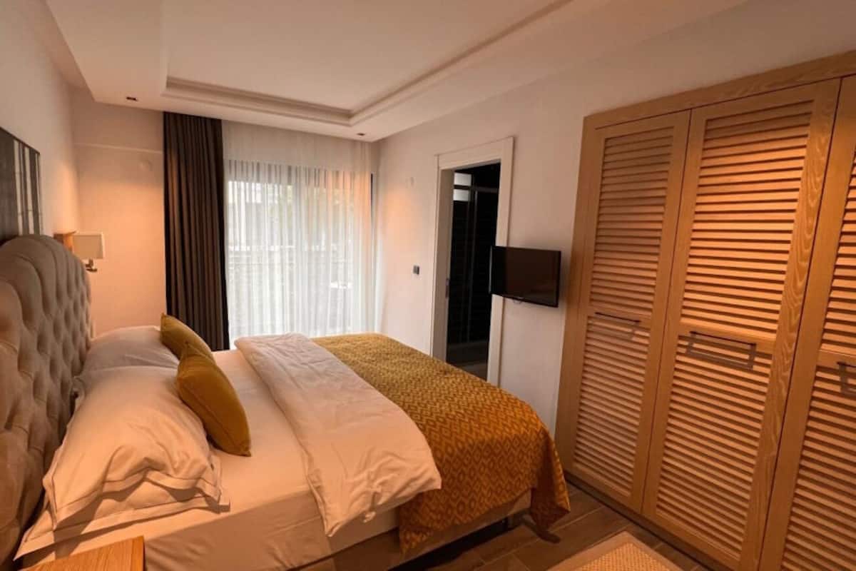 A hotel room with a bed, a wardrobe, a TV, and a window with curtains.