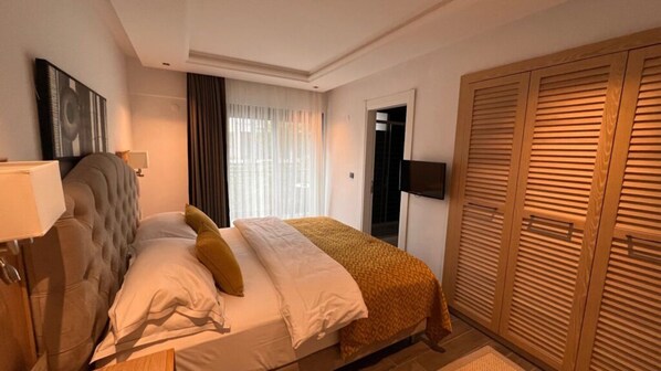 Een hotelkamer met een bed, een kledingkast, een televisie en een raam met gordijnen.