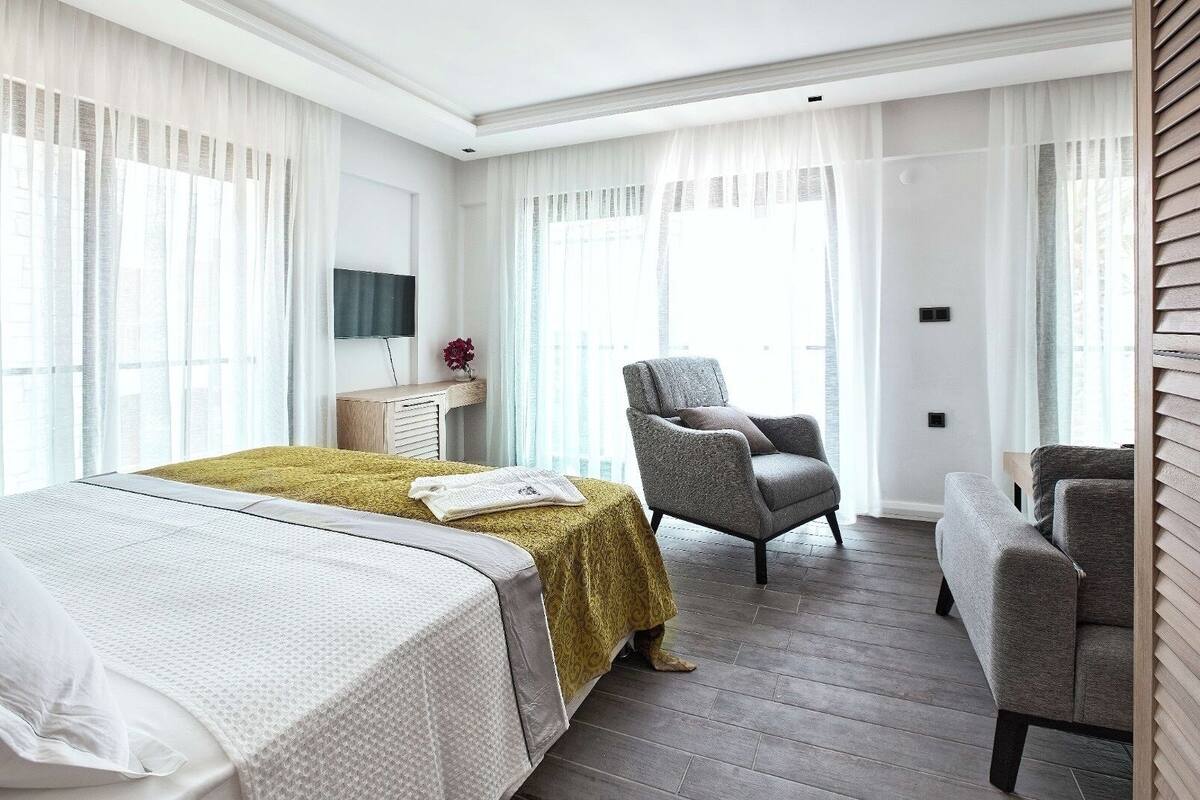 A hotel room with a bed, two armchairs, a desk, and a television.