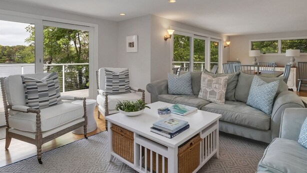 A spacious living room with a large window, a white coffee table, and two sofas with patterned cushions. - Crystal Lake Waterfront Cottage (Orleans)