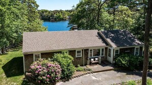 A single-story house with a brick exterior, a covered porch, and a view of a lake. - Crystal Lake Waterfront Cottage (Orleans)