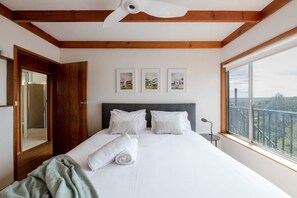 Ein Schlafzimmer mit einem großen Bett, Holzbalkendecke, einem Fenster mit Blick und drei gerahmten Bildern an der Wand.