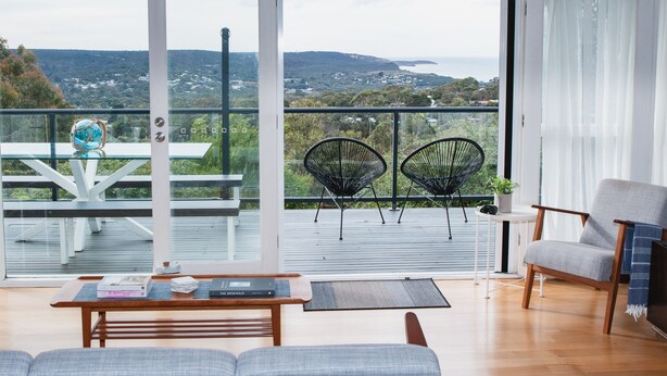 Uma sala de estar moderna com uma grande porta de vidro que dá para uma varanda com vista panorâmica.