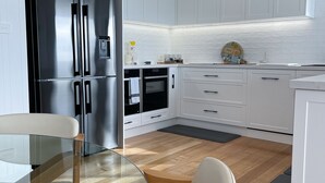Uma cozinha moderna com armários brancos, uma geladeira de aço inoxidável, uma mesa de jantar de vidro e piso de madeira.