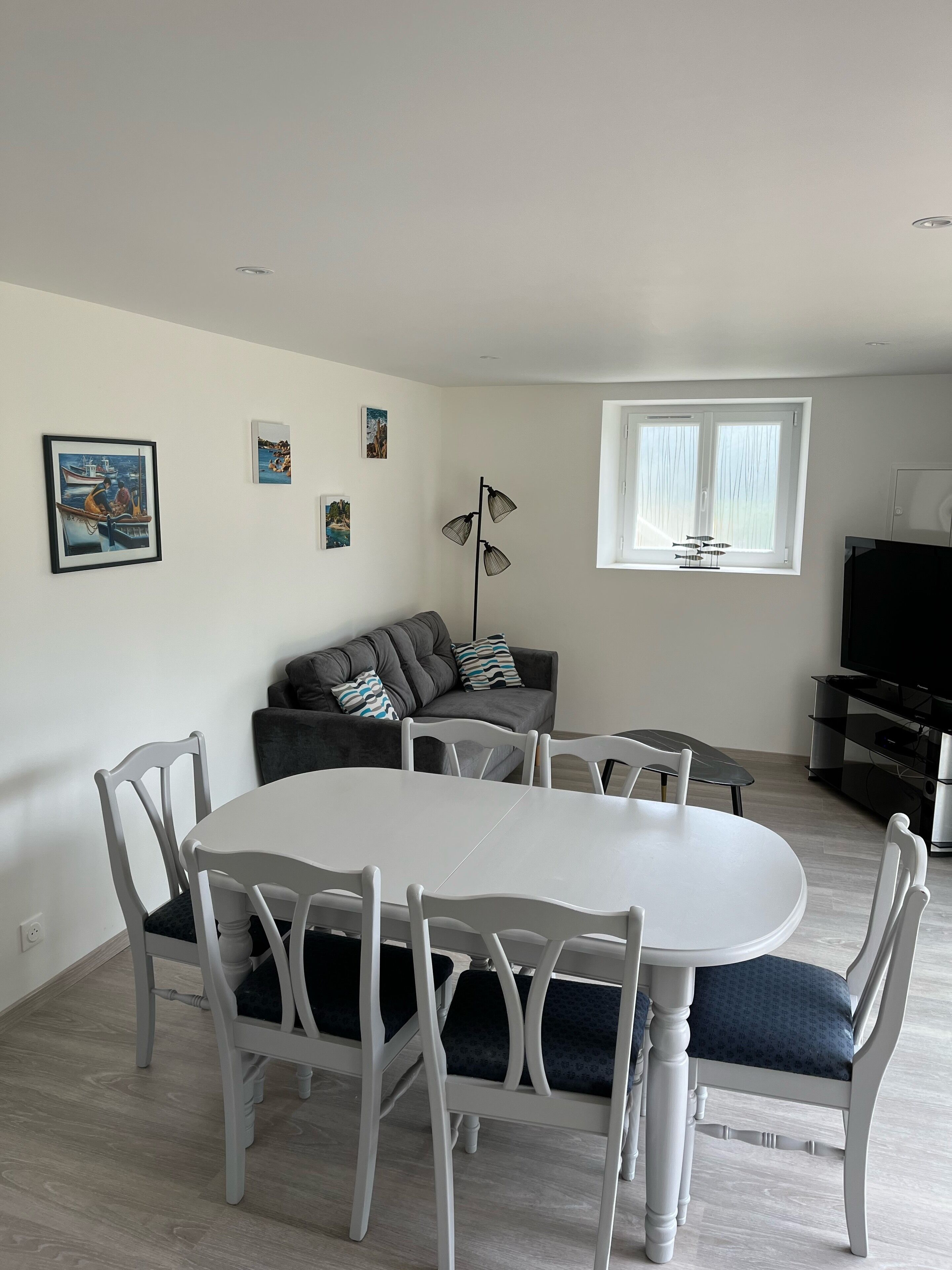 Un salon moderne avec une table à manger, des chaises blanches, un canapé gris et un lampadaire.