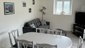 A modern living room with a dining table, white chairs, a grey sofa, and a floor lamp. - APARTMENT "ILE BONO" WITH GARDEN, 800 ml BEACH (Perros-Guirec)