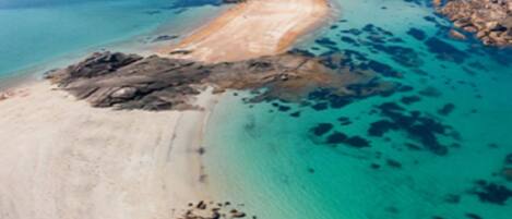 An aerial view of a coastal area with clear turquoise waters, sandy beaches, and rocky outcrops.