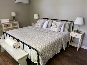 A neatly made bed with striped bedding, two bedside tables with lamps, and a small bedside table with a rolled towel. - Lakefront • Hot Tub • Private Dock • Kayaks • Canoe • Fire Pit • Dog Friendly (Coolbaugh Township)