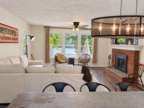 A living room with a sofa, chairs, a dining table, a fireplace, and a view of a body of water through large windows. - Lakefront • Hot Tub • Private Dock • Kayaks • Canoe • Fire Pit • Dog Friendly (Coolbaugh Township)