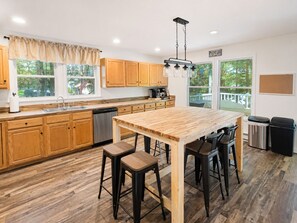 Une cuisine avec des meubles en bois, un îlot central doté de tabourets, un lave-vaisselle et une vue sur l’extérieur.