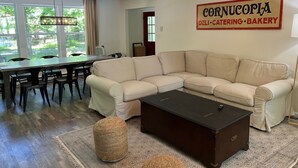 A living room with a sectional sofa, a dining table, and a sign for Cornucopia deli, catering, and bakery. - Lakefront • Hot Tub • Private Dock • Kayaks • Canoe • Fire Pit • Dog Friendly (Coolbaugh Township)