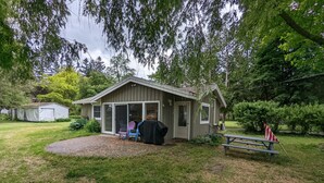 Een klein houten huisje met een overdekte veranda, een picknicktafel en een barbecue.