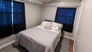 Een slaapkamer met een bed, twee ramen met gordijnen, een houten plafond en een vloerbedekking.
