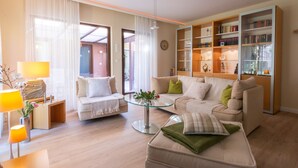 A modern living room with a sofa, ottoman, and a glass coffee table. There is a bookshelf filled with books and decorative items. - Exclusive vacation home in the Dichterviertel (Brück)