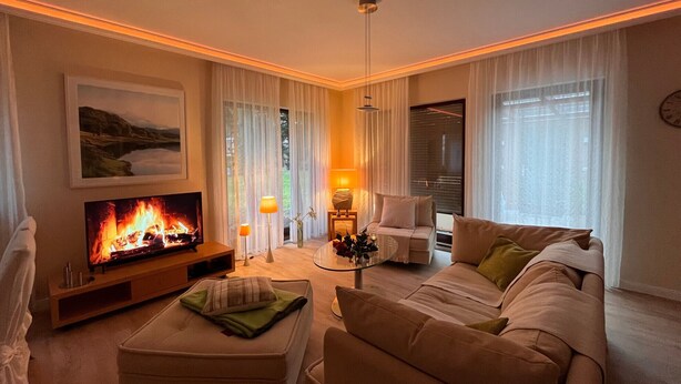 A cozy living room with a flat-screen TV, a comfortable sofa, a glass coffee table, and a fireplace. - Exclusive vacation home in the Dichterviertel (Brück)