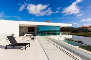 A modern outdoor terrace with a pool, lounge chairs, and a glass-enclosed dining area.