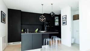 Een moderne keuken met zwarte kastjes, een centraal eiland en een eetgedeelte met transparante stoelen.